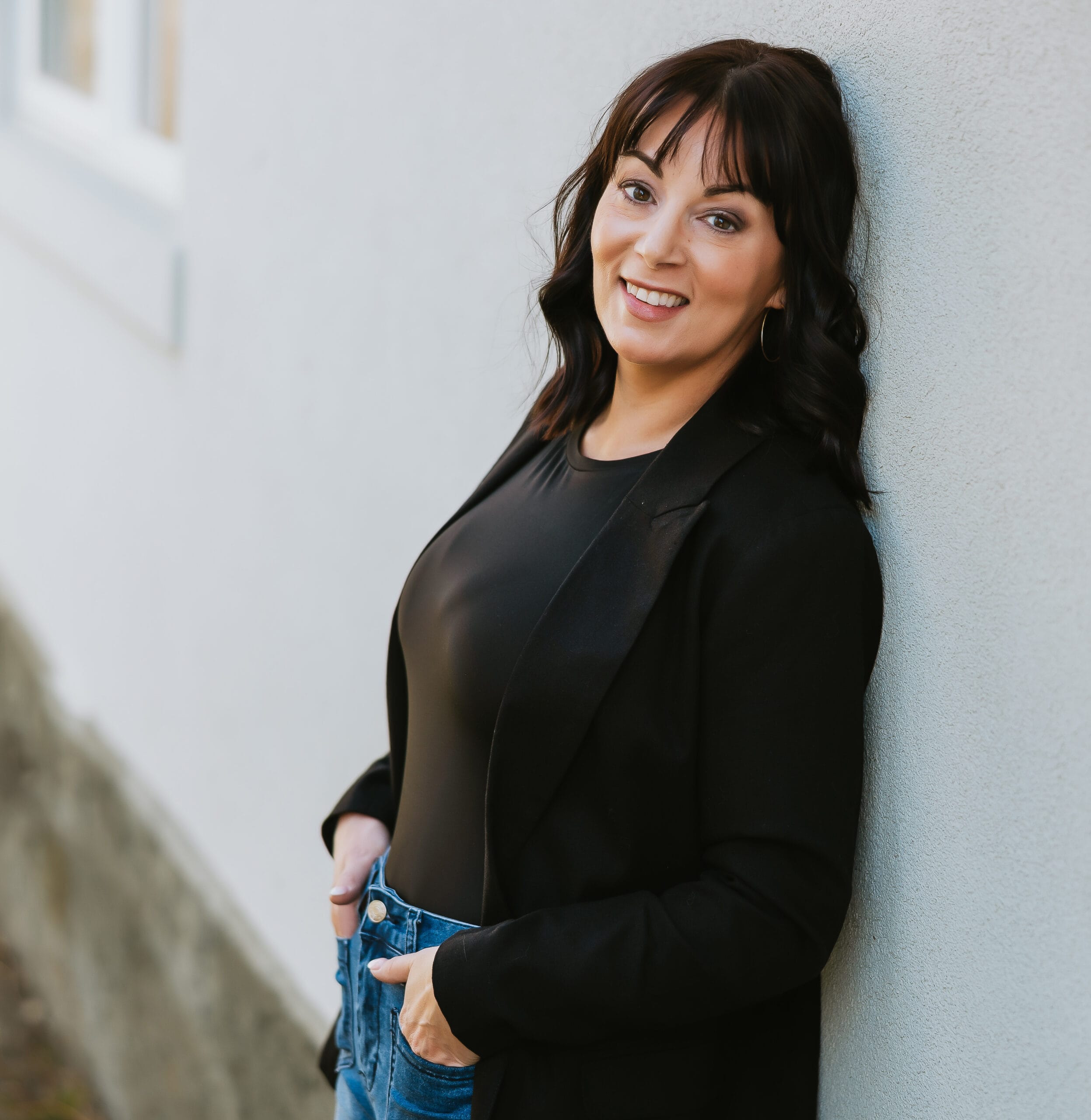 Stacey Steele leaning against a wall outside smiling warmly.